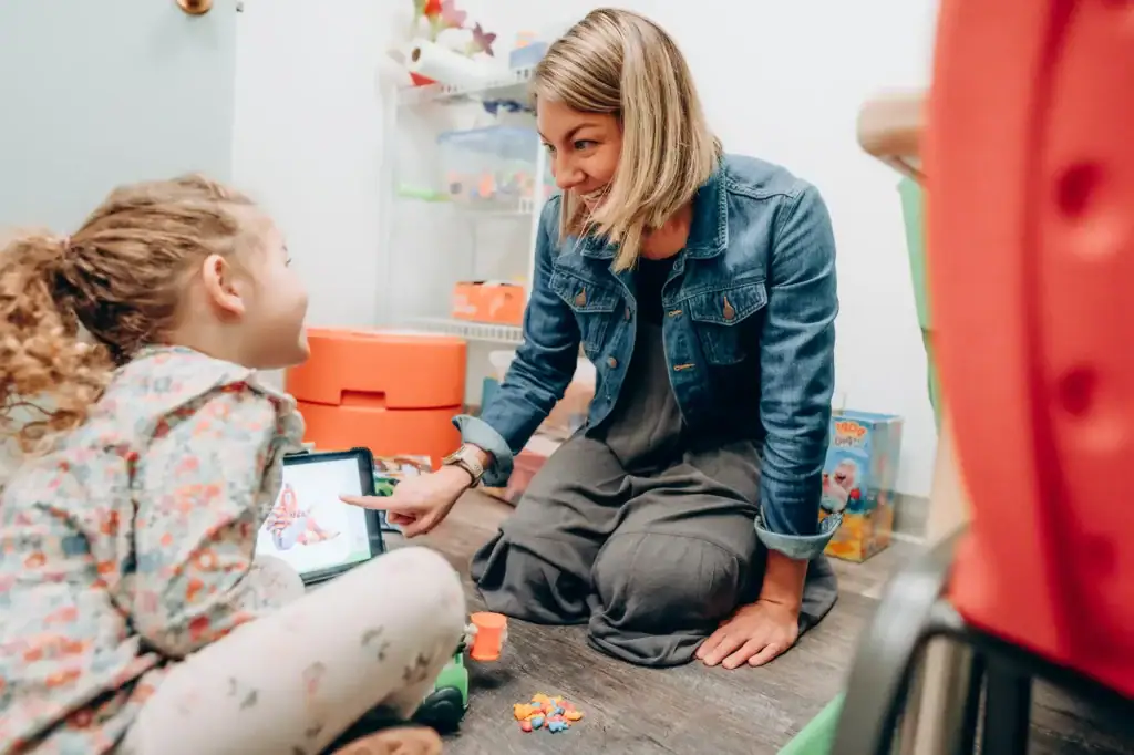 Empathetic speech therapist working with a young girl using a tablet during speech therapy session at Speech Therapy Solutions Montana.